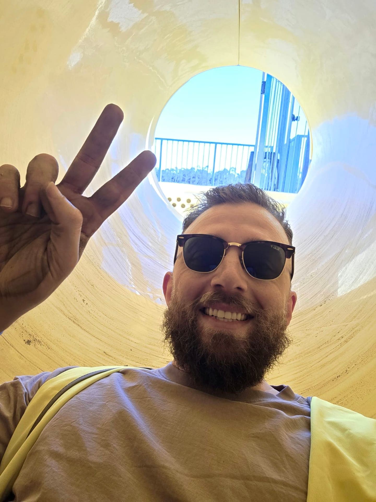 Adrian, founder of REST Group, smiling inside an enclosed waterslide flume during an inspection, the flume opening and the start tower behind him