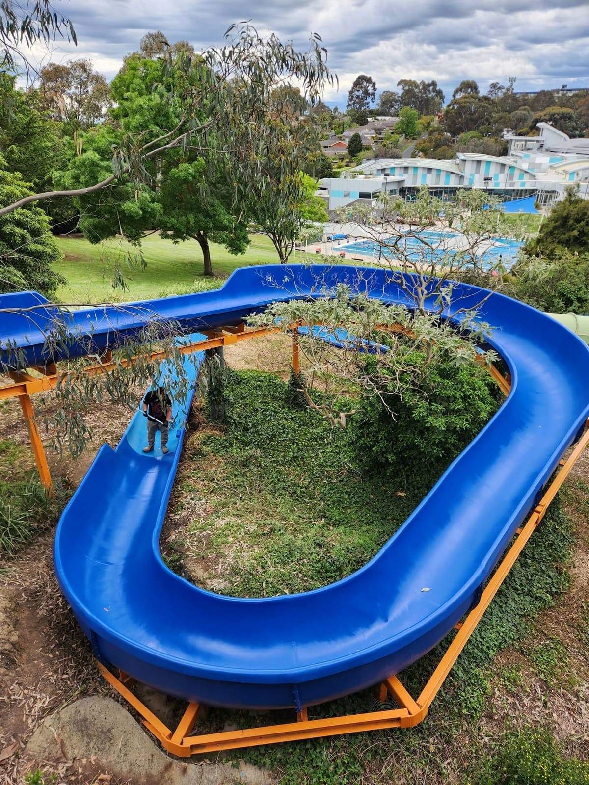 A REST inspector standing in a blue body slide run that loops through the trees above a public pool complex